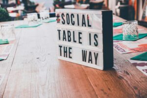 su un tavolo di legno è appoggiato un cartello bianco con su scritto: il tavolo sociale è la strada